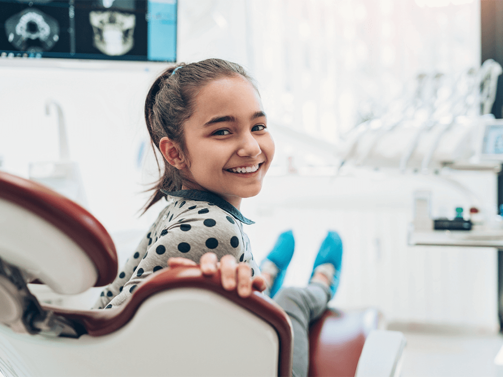 Image of a woman in a dental chair, smiling while holding a toothbrush.