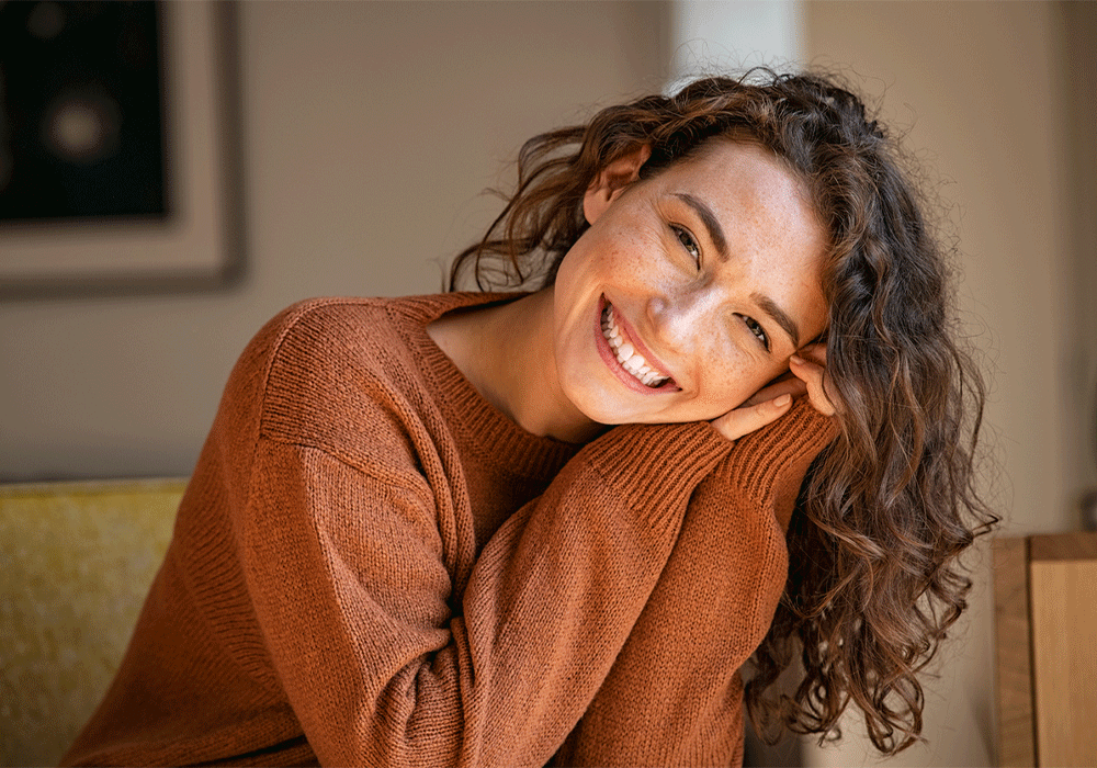 Image of a woman smiling and resting her head on her hands, representing a relaxed and happy dental patient.